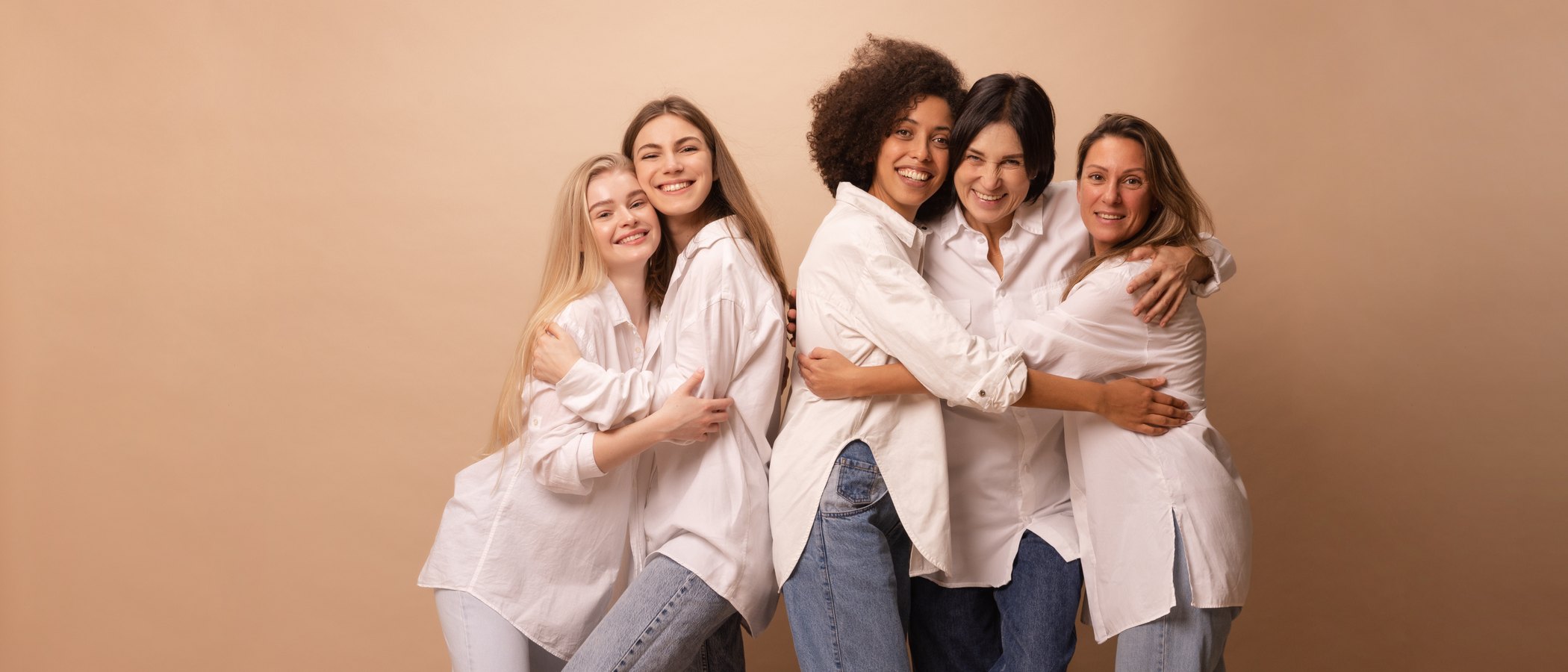 A group of women together, relaxed and smiling, neutral warm background